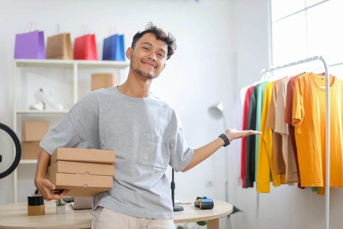 An entrepreneur holding parcels beside a rack of products ready to sell